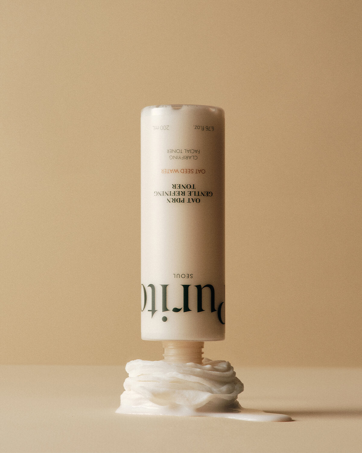 An upside-down toner bottle resting its opening on a swirl of thick, white cream against a tan background