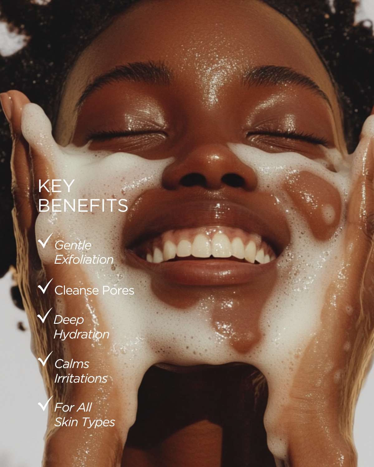 Woman smiling with white facial foam on her face. Benefits include gentle exfoliation and deep hydration.