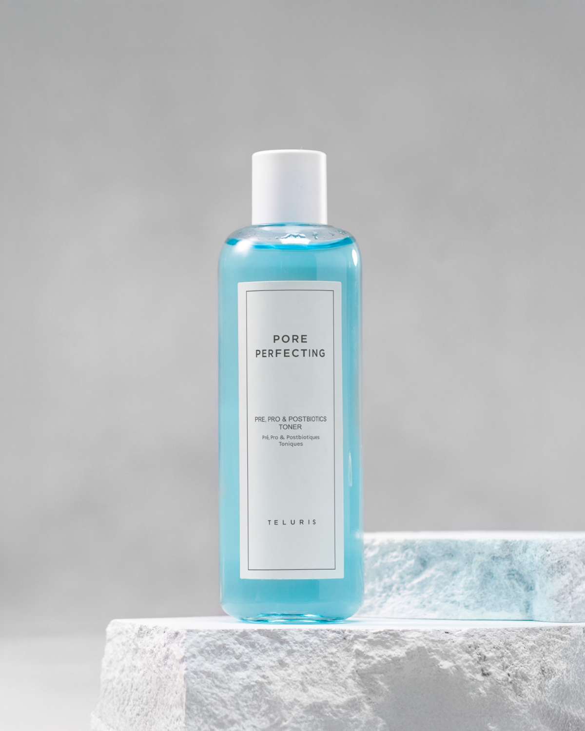 Blue Teluris Pore Perfecting Toner bottle displayed on a white stone pedestal.