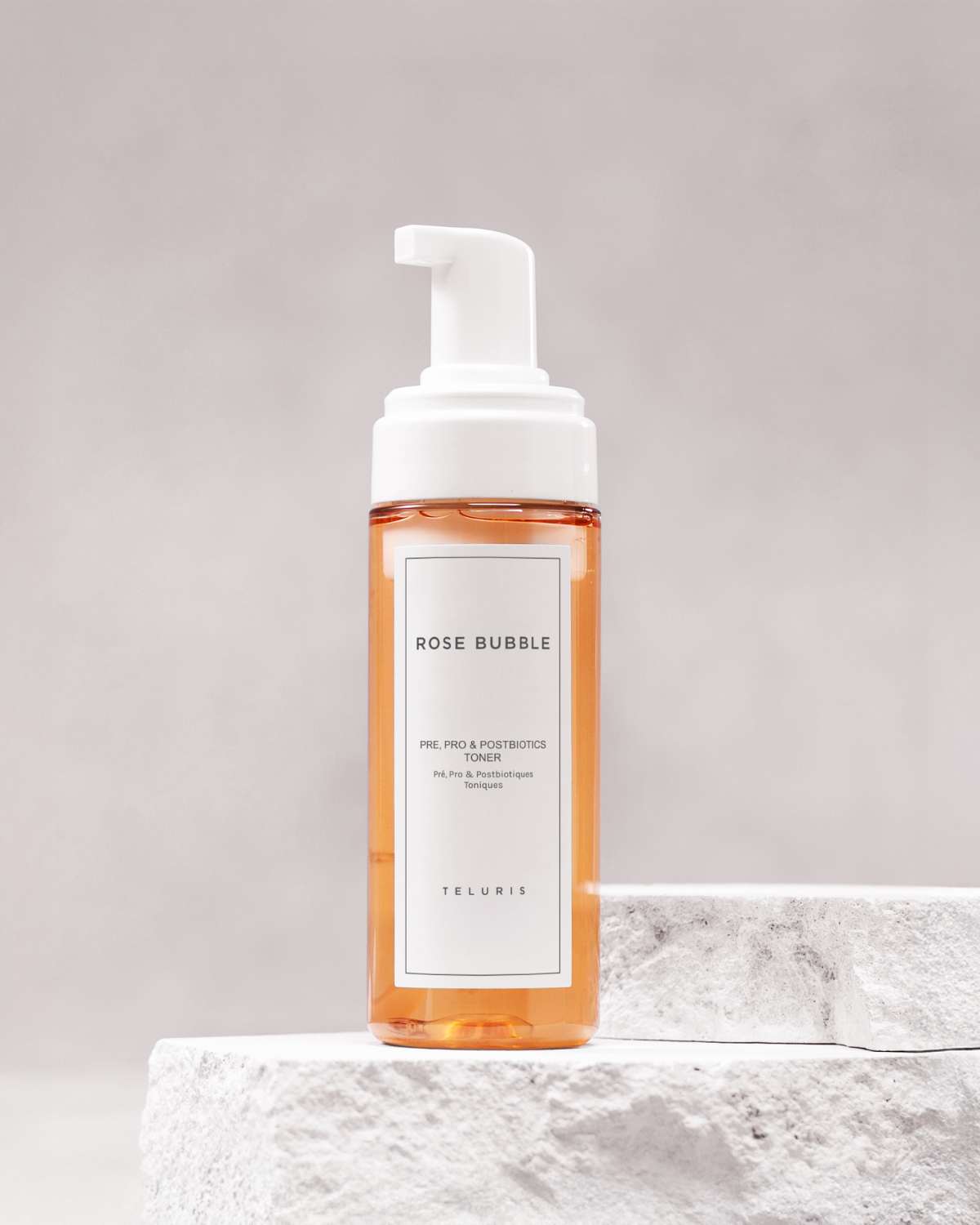 Pink Teluris Rose Bubble Toner bottle on a white stone pedestal with a clean grey background.