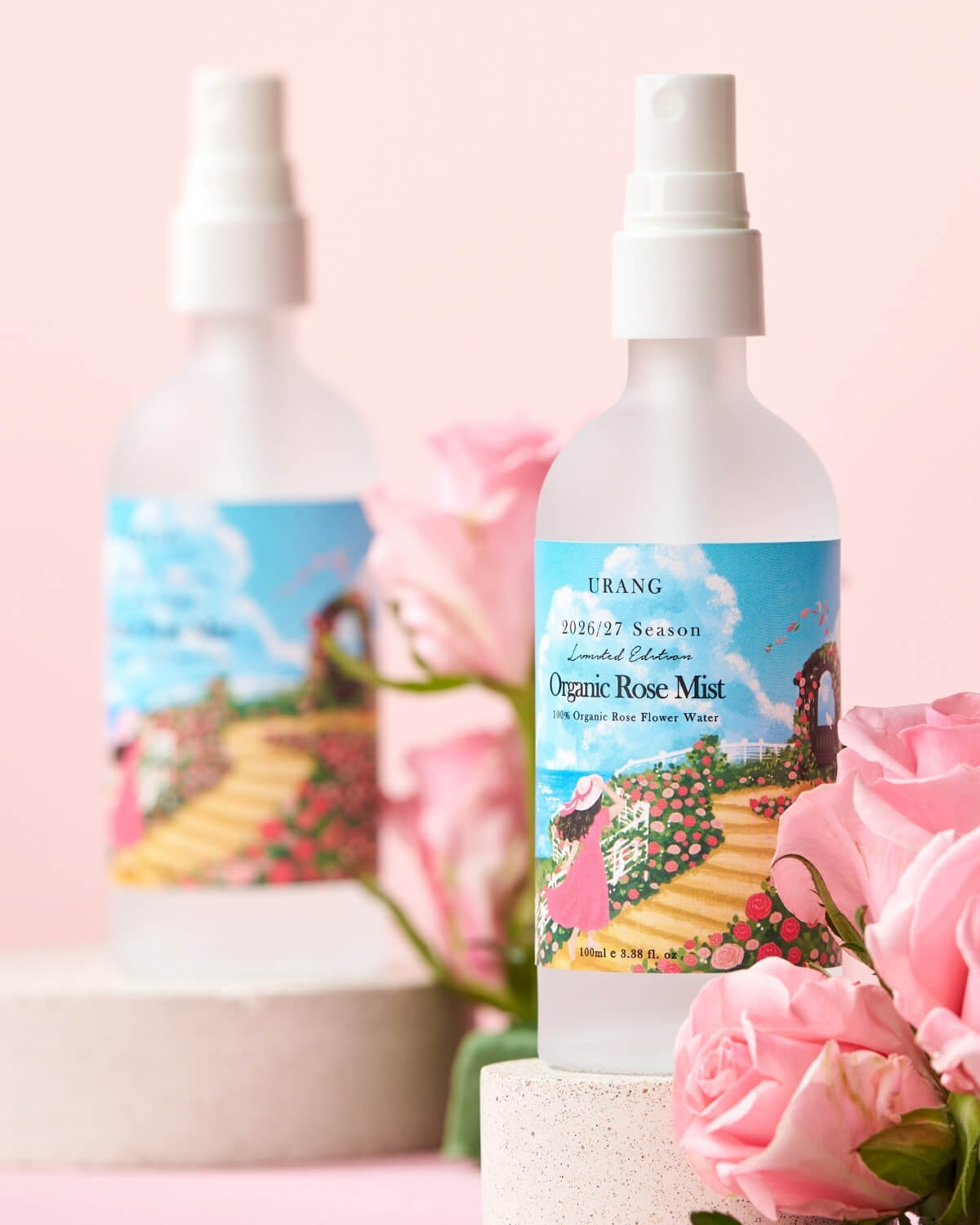 URANG Organic Rose Mist bottle display on a stone pedestal with soft pink roses on a pink background.