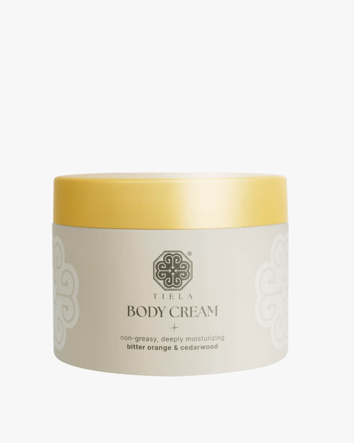 Front view of a round Tiela Body Cream jar in beige with a bright yellow lid, labeled "non-greasy, deeply moisturizing bitter orange & cedarwood."