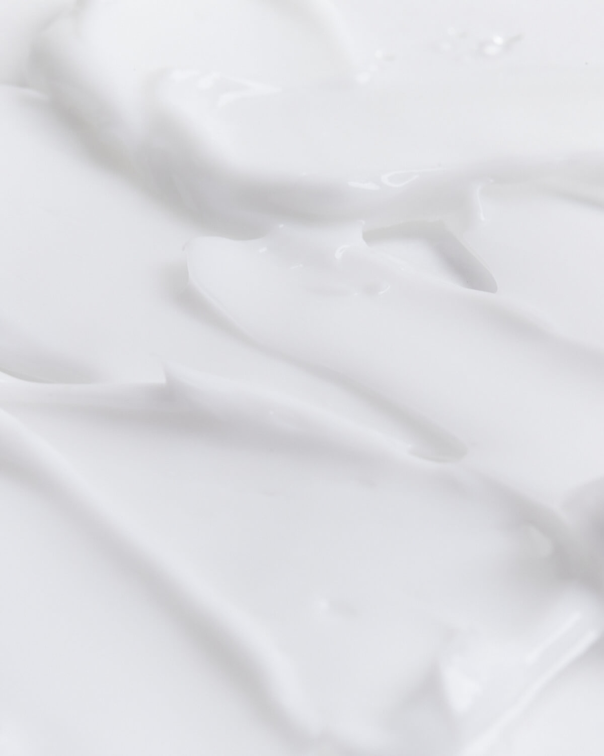 Extreme close-up of a white, creamy texture, showing thick, smooth swaths and peaks, representing the body cream product.