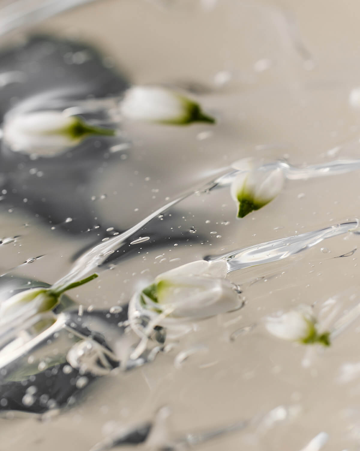 An extreme close-up, abstract shot of white floral buds, possibly neroli, submerged and suspended within a clear, glistening gel or balm product.