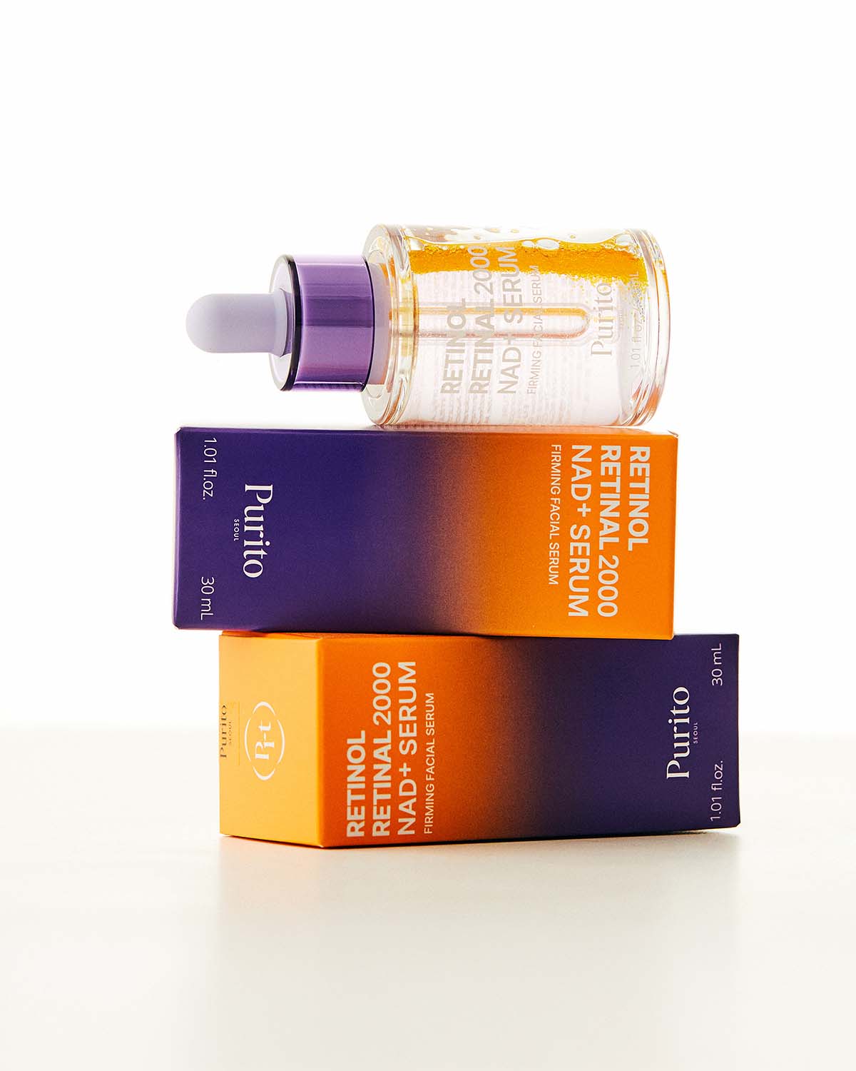 A Purito Retinol serum bottle resting on top of two stacked purple and orange product boxes.