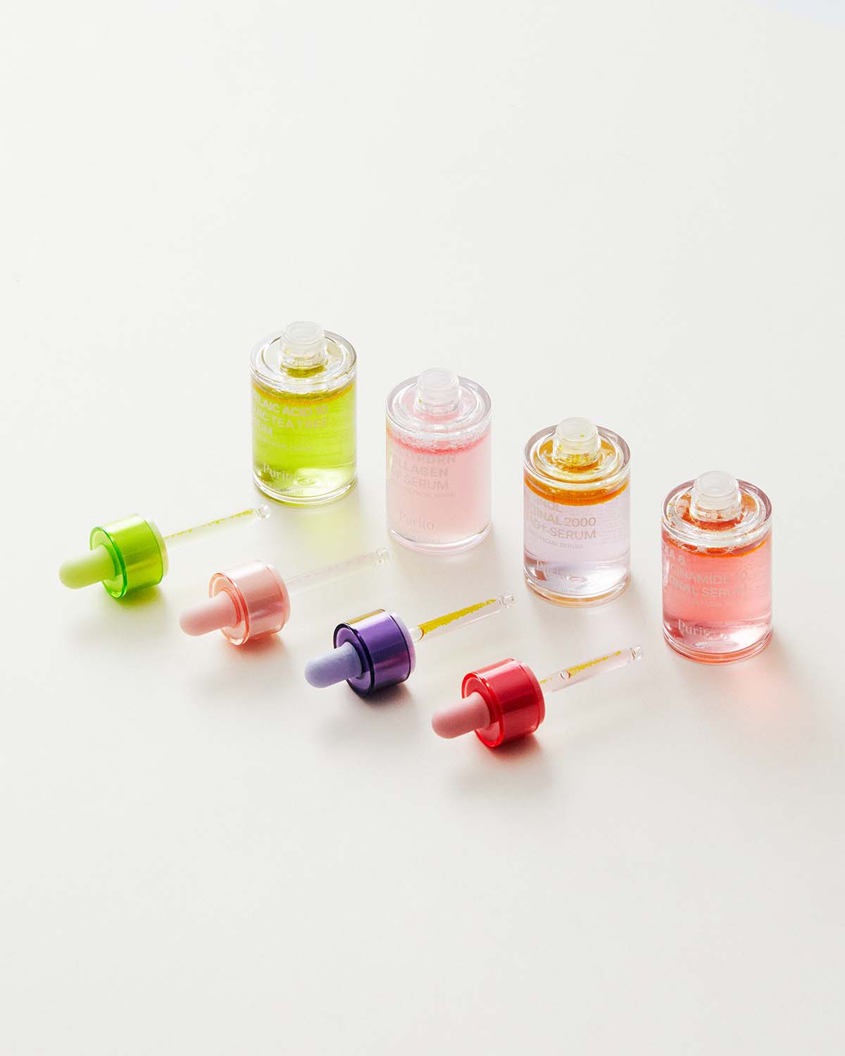 Four different Purito facial serums in glass bottles with colorful dropper caps on a white surface.
