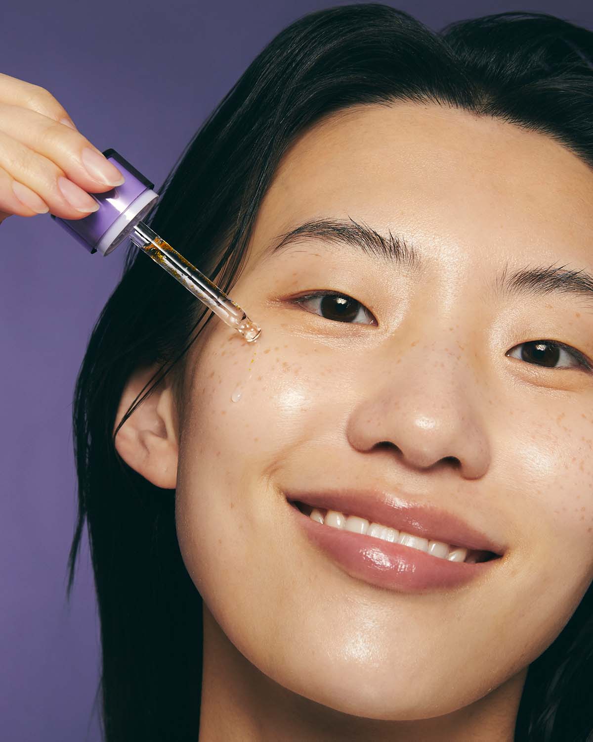 Smiling model applying a drop of Purito Retinol Retinal 2000 NAD+ Serum to her cheek.