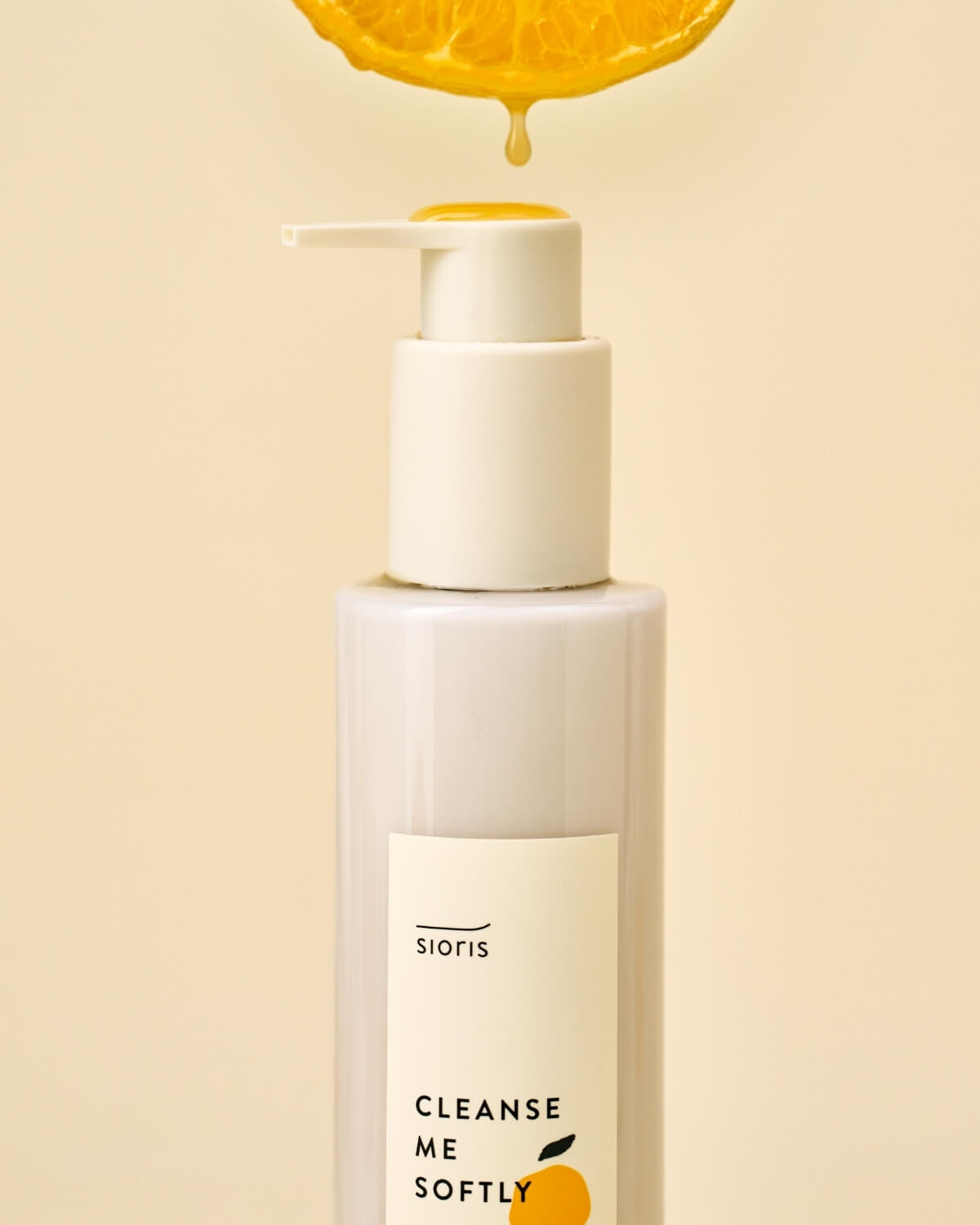Close-up of the cleanser pump with a yellow oil drop falling from a citrus slice above.