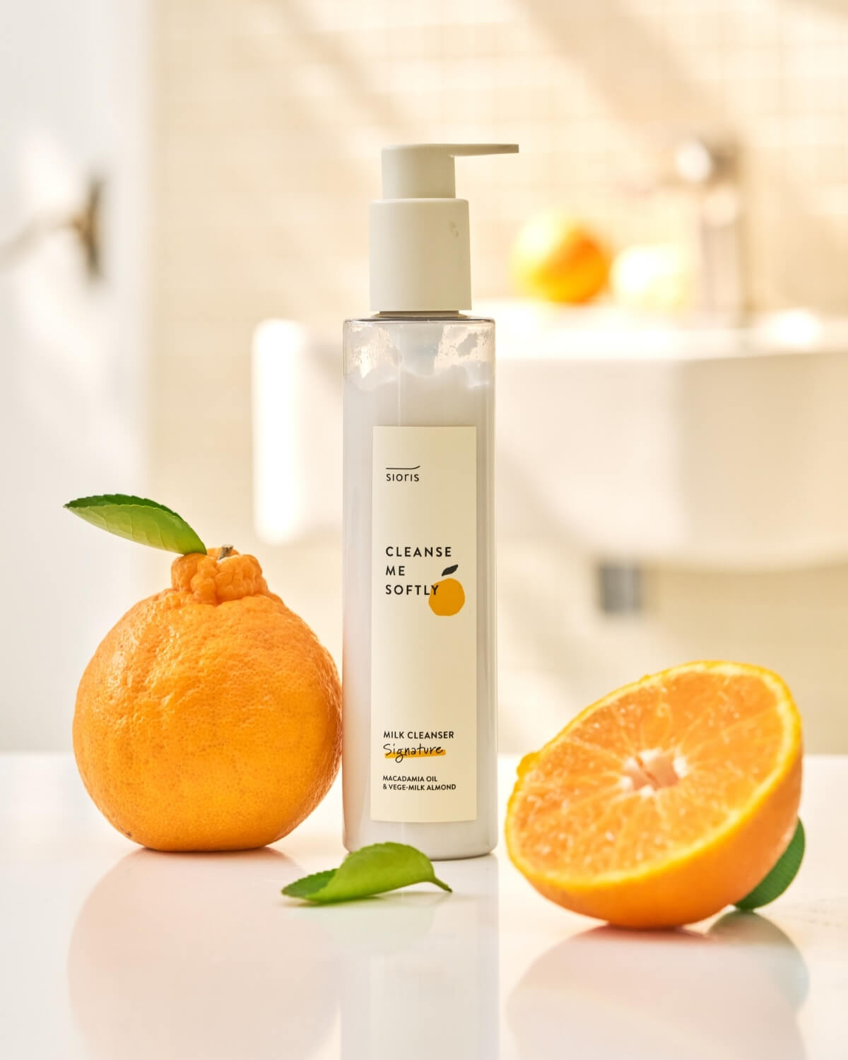 Sioris milk cleanser bottle on a counter next to fresh citrus fruit in a bright bathroom setting.