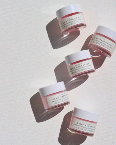 Five small jars of TeraCell Skin Dewy Hydration face cream arranged diagonally on a white textured background with strong sunlight and shadows.
