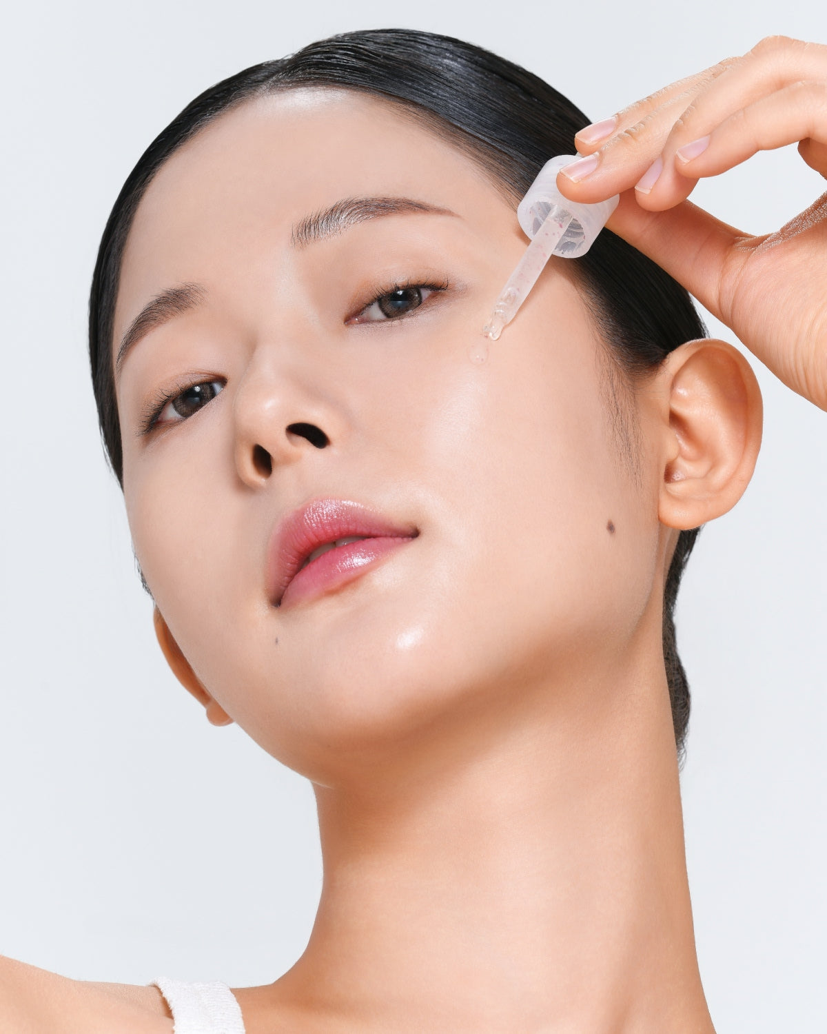 A close-up of a person applying a clear liquid from a dropper onto their cheek.