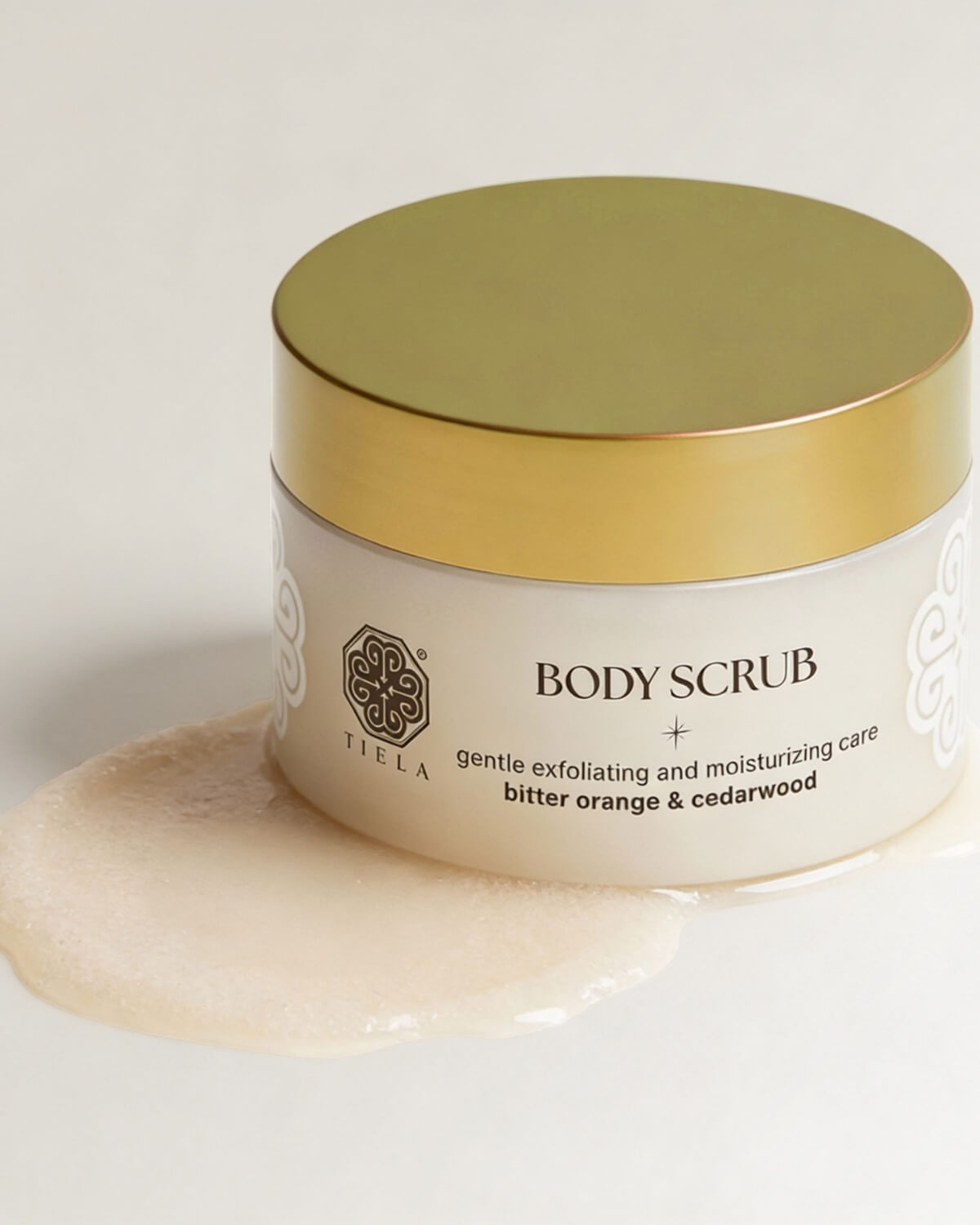 A jar of Tiela Bitter Orange & Cedarwood body scrub sitting on a large, textured product smear.