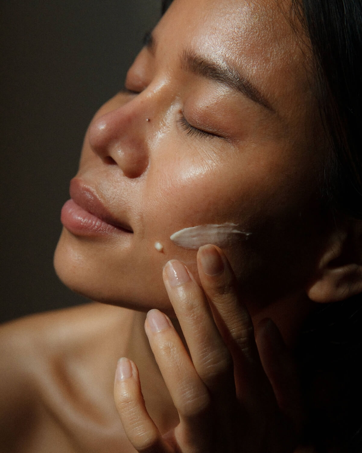 Close-up of a woman applying the creamy WYLYS New Day Glow serum to her face for skin brightening.