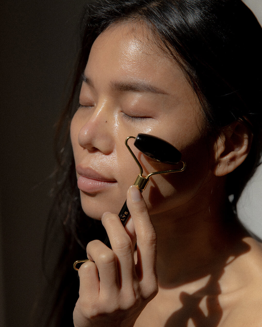 WYLYS Black Obsidian Face Roller on Model face demo. Depuff, cool, relax, facial tool made with 100% natural black obsidian and metal in gold.