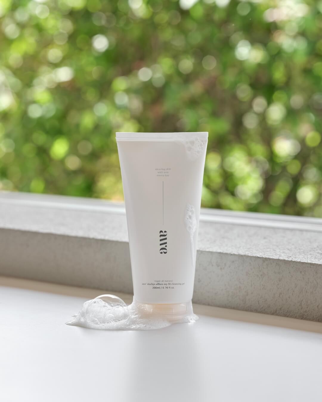 Awe face cleansing gel tube with soapy bubbles on a window sill with green trees background.