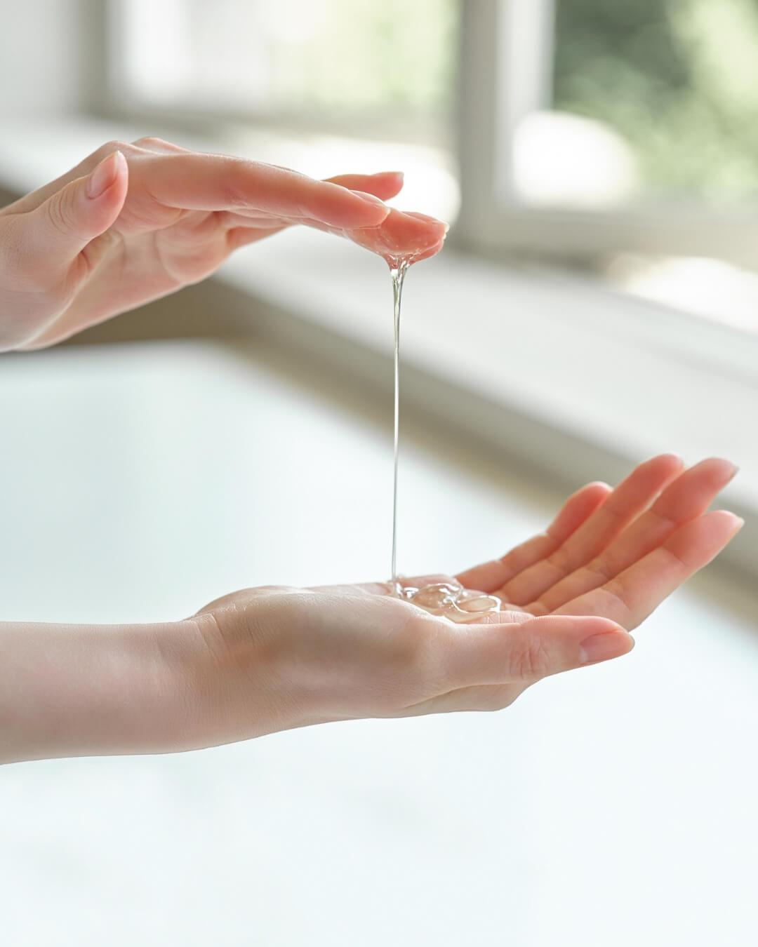 Close-up of clear, dynamic liquid gel cleanser stretching between a woman's hands.