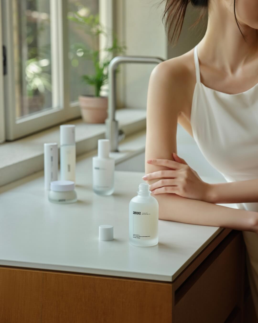 Open bottle of Awe daily essence toner on a white kitchen counter next to a woman.