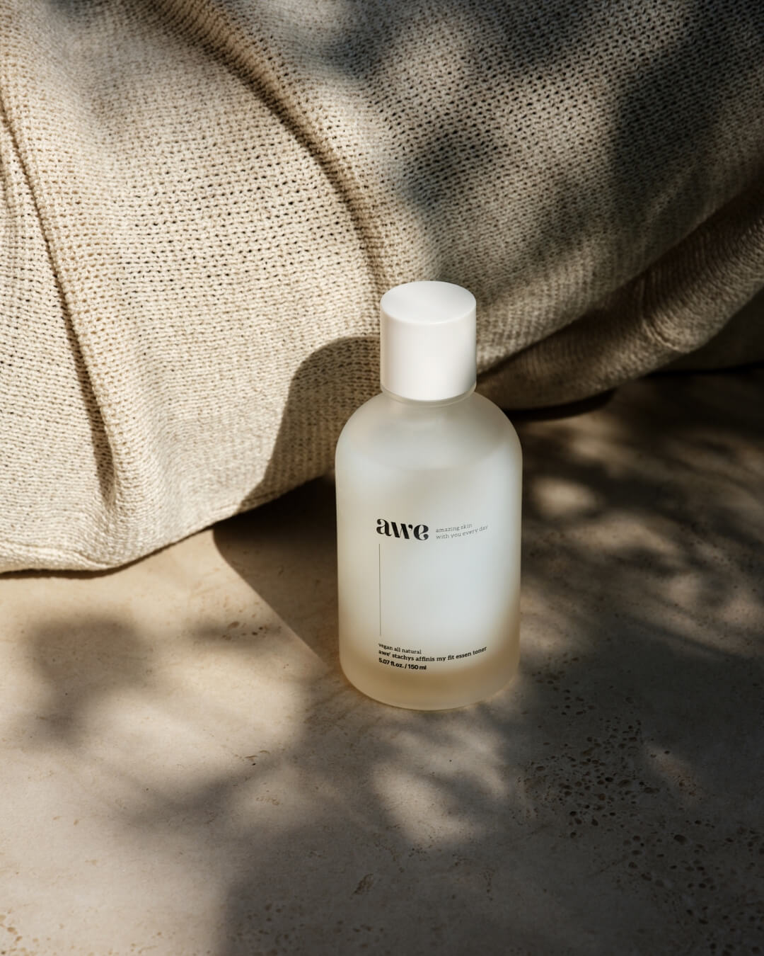 Awe natural essence toner bottle on stone tile next to a beige knit sweater.
