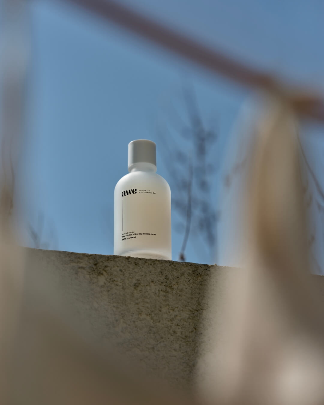 Awe daily hydrating essence toner bottle sitting on a concrete wall under a clear blue sky.