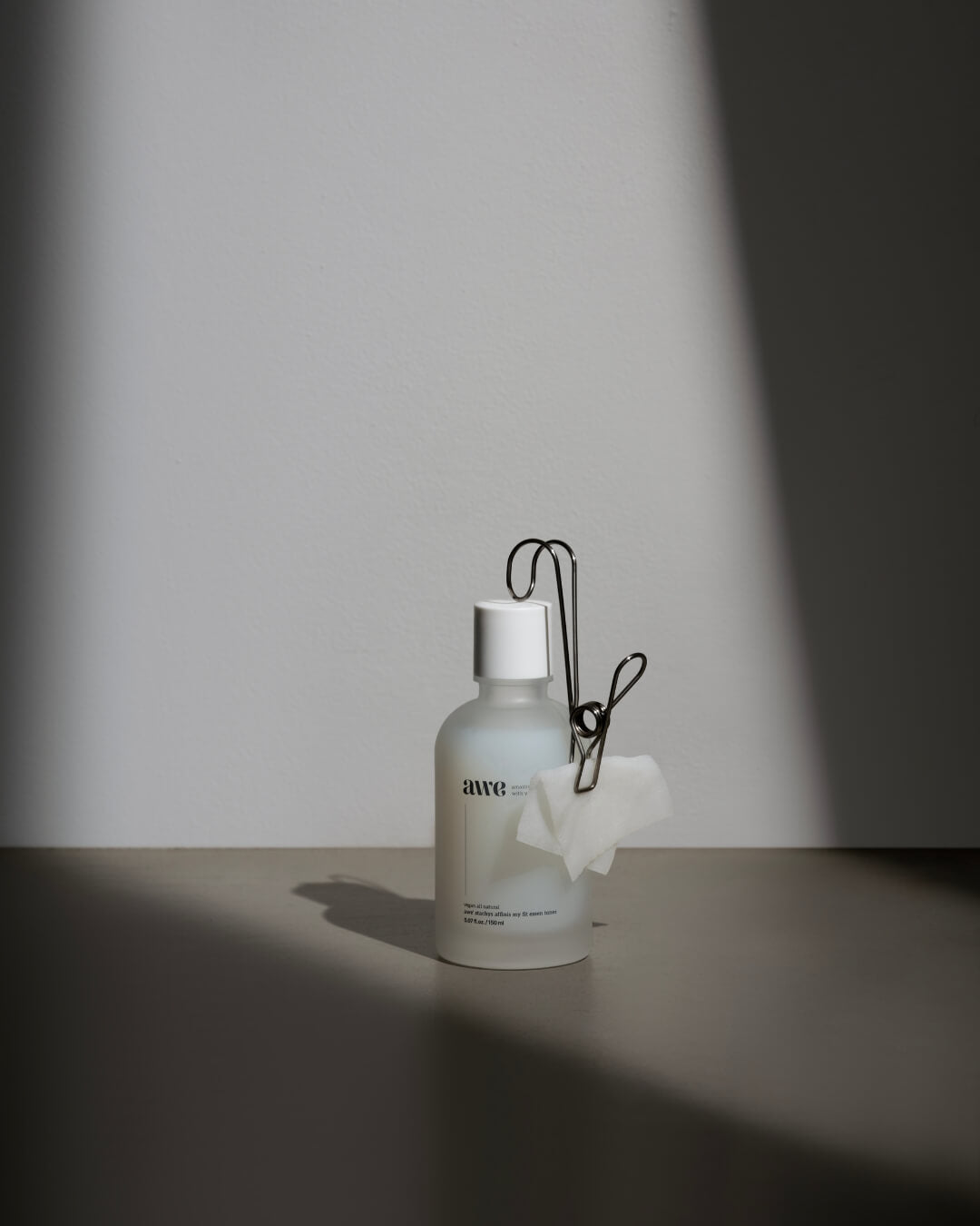 Awe face essence toner bottle with a metal clip and cotton pad in dramatic studio lighting.