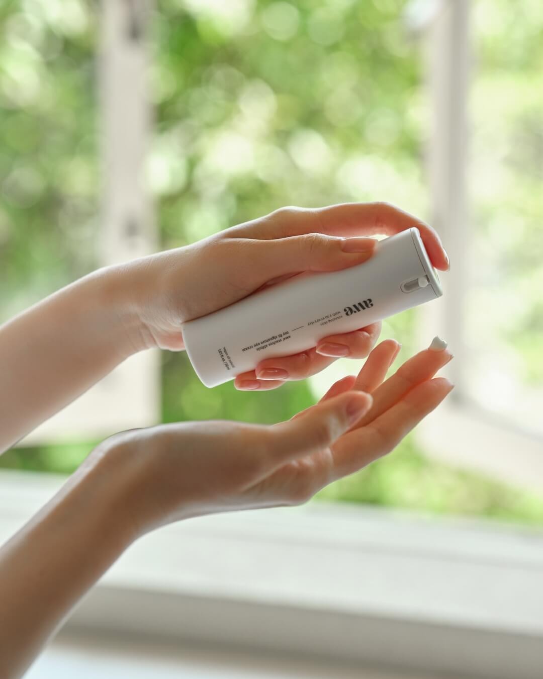 Close-up of a woman pumping white cream from an Awe natural eye cream bottle onto her fingertip.