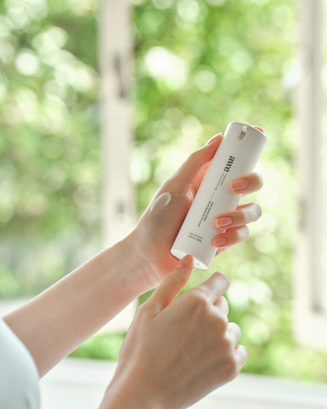 Woman holding an Awe firming eye cream bottle with a product swatch on the back of her hand.