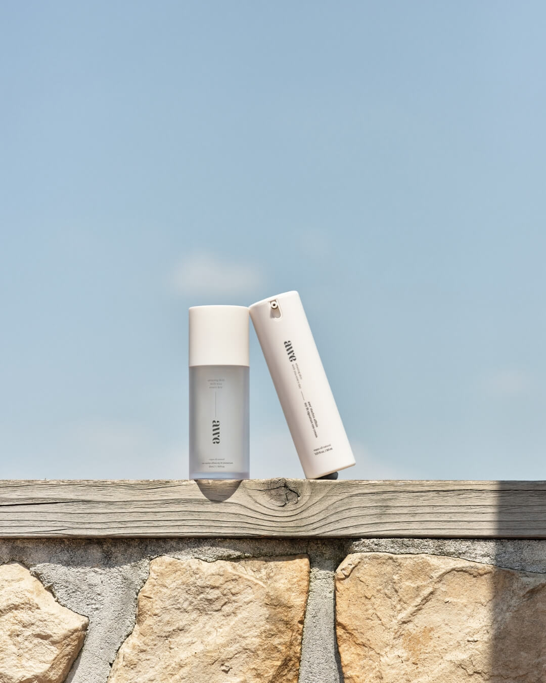 Awe anti-aging eye cream bottle leaning against a tall skincare bottle on an outdoor stone wall.
