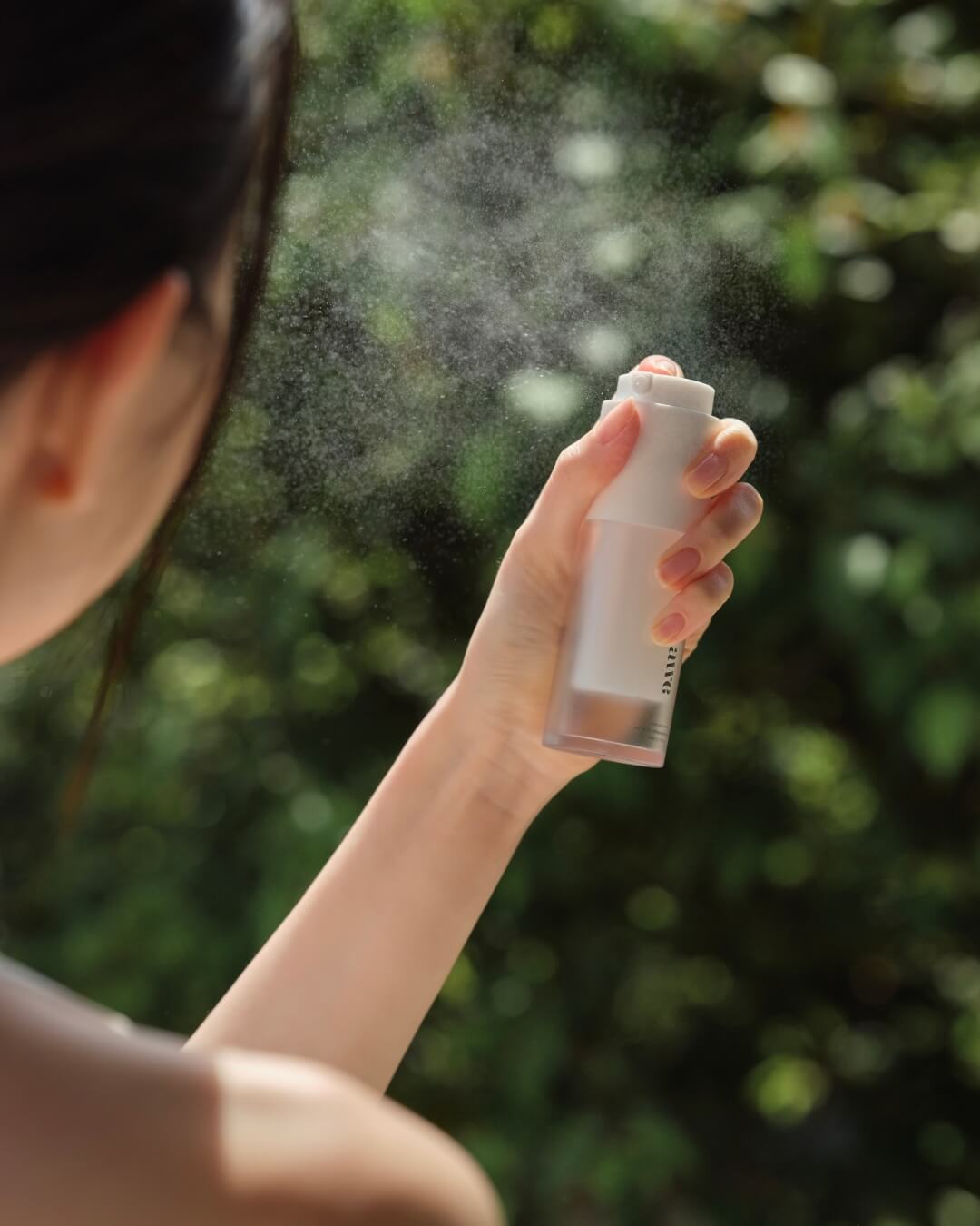 Close-up of a woman spraying Awe face mist serum creating a fine refreshing mist outdoors.