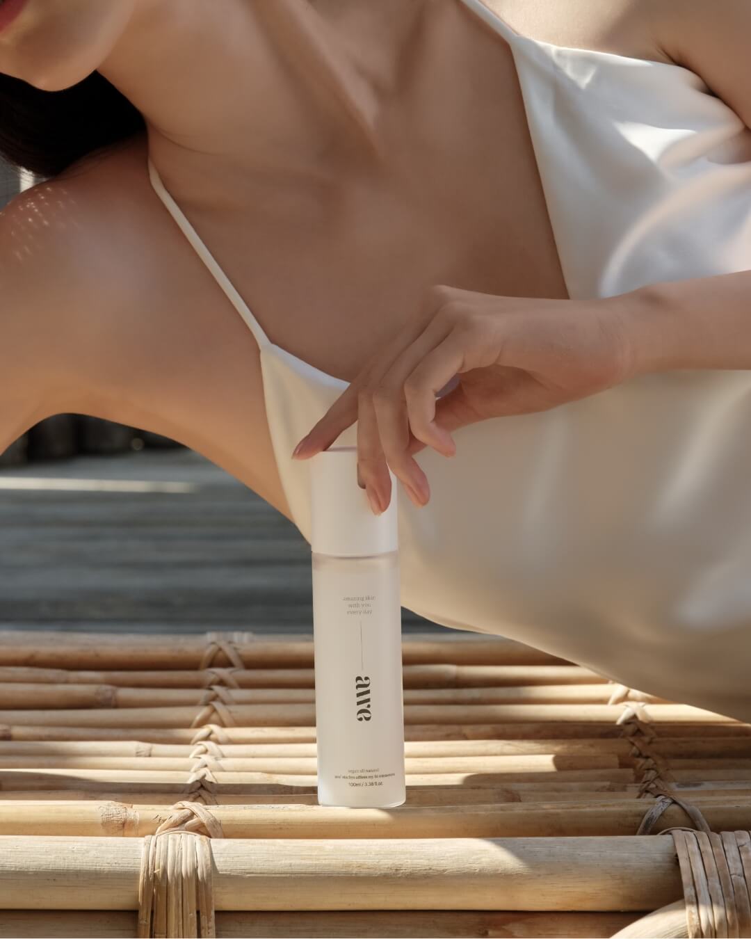 Woman resting on a bamboo mat next to a bottle of Awe natural firming mist serum.