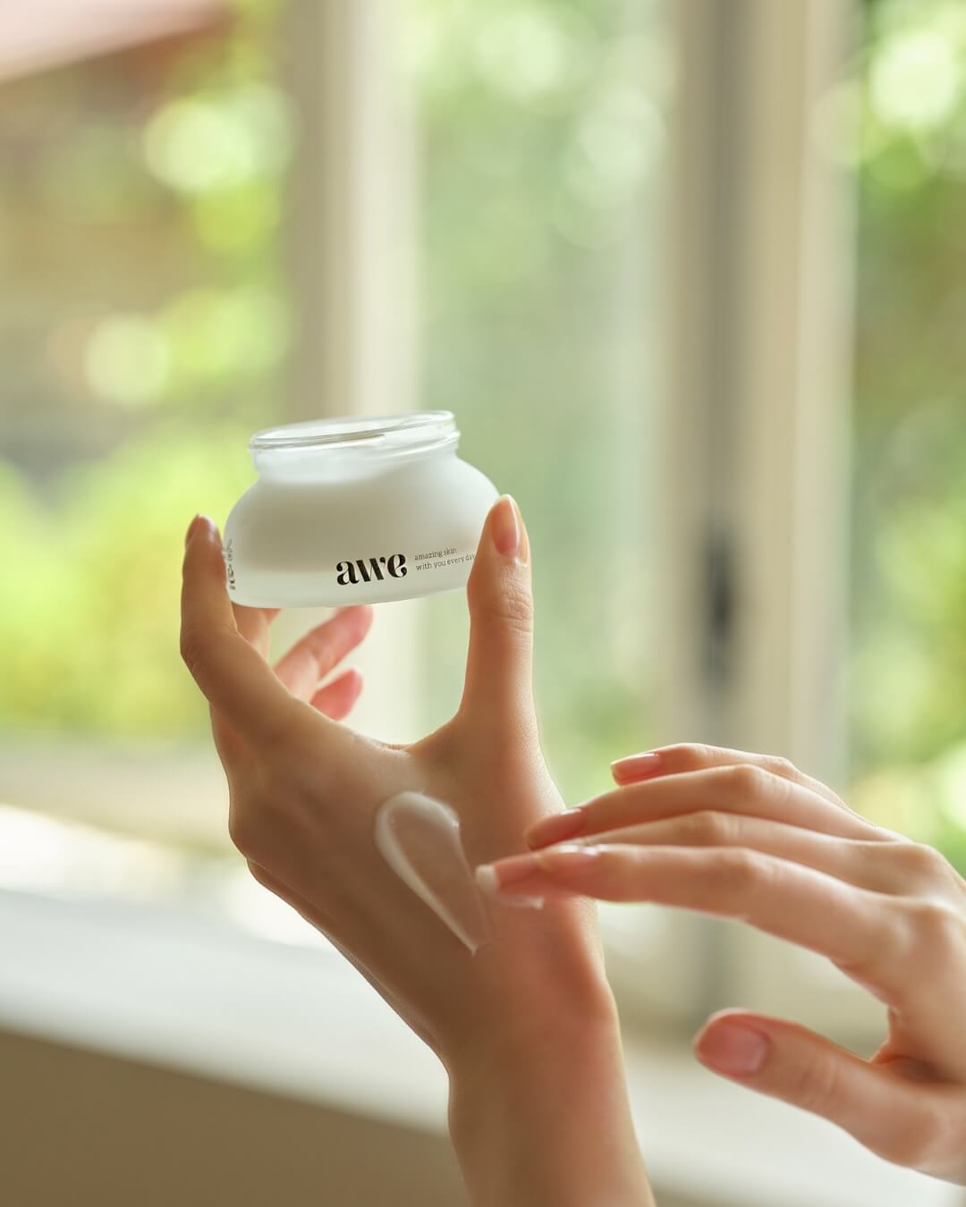 Close-up of a woman applying a swatch of Awe radiance cream onto the back of her hand.