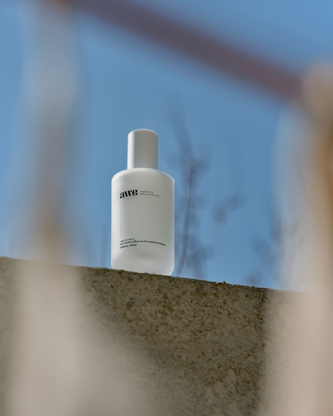 Awe daily soothing emulsion bottle resting on a concrete ledge under a bright blue sky.