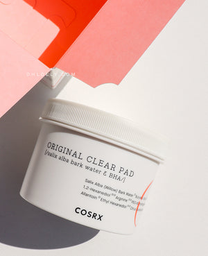Cosrx One Step Original Clear Pad Cosrx Original Clear Pad tub with BHA and Willow Bark Water ingredients, next to its packaging on an orange background.
