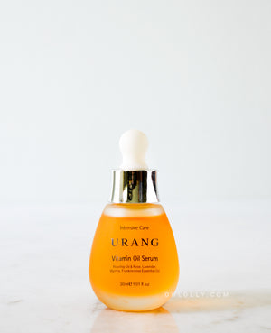 The Urang Vitamin Oil Serum in a frosted glass dropper bottle with a white and gold cap, showcasing the yellow-orange oil, sitting on a light marble surface against a white background.