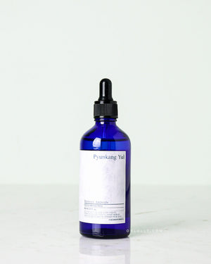 Studio shot of the Pyunkang Yul Moisture Ampoule. The rich, honey-like gel is contained in a dark blue glass jar, with the dropper resting on the rim, against a pale white background.